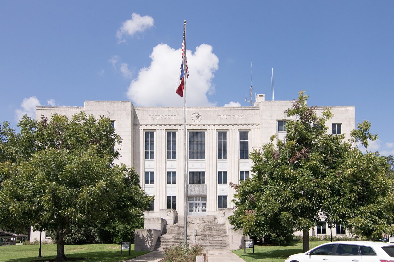 Brazoria County Courthouse in Angleton, a pale stone Art Deco building behind trees, with a flagpole at the steps.